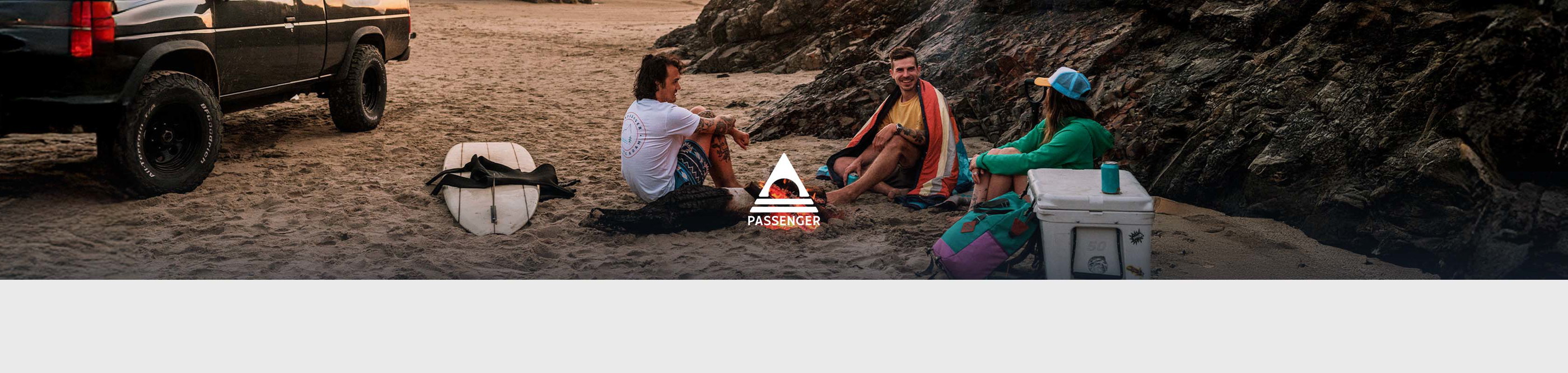 Shop Passenger collection. A group of surfers sitting around campfire on the beach